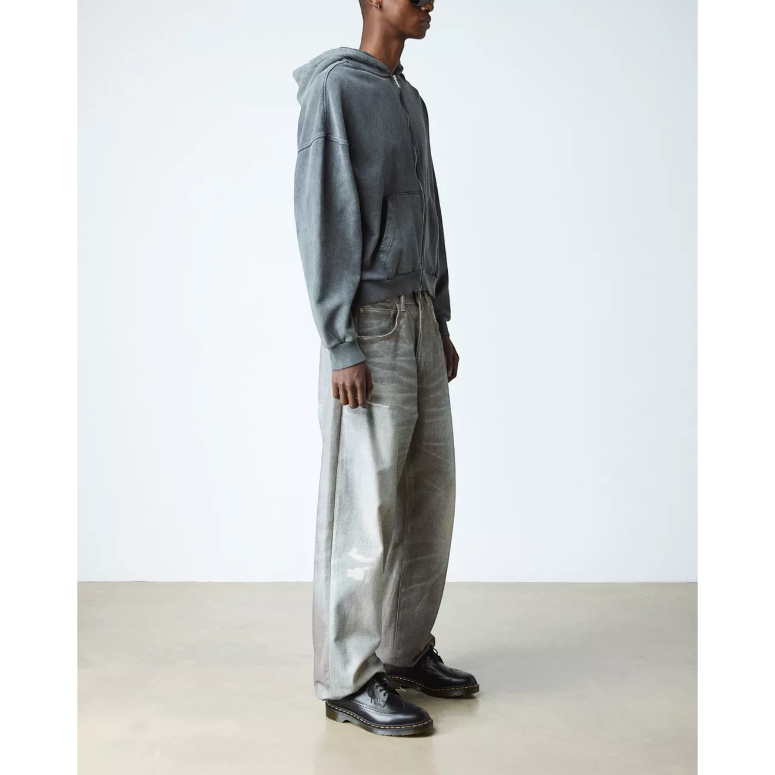 My Store black smooth leather brogue shoes with wingtip detailing and PVC sole. Model wears them with grey jeans and a charcoal zip-up hoodie.