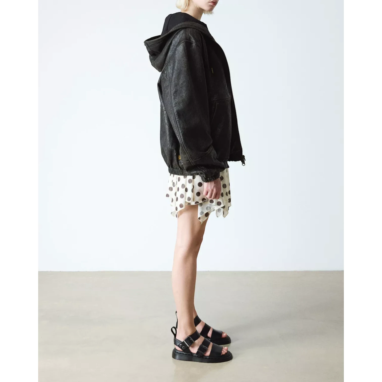 My Store black Gryphon Brando leather hooded jacket with a slightly textured finish, worn by a model with a polka dot dress and black sandals.