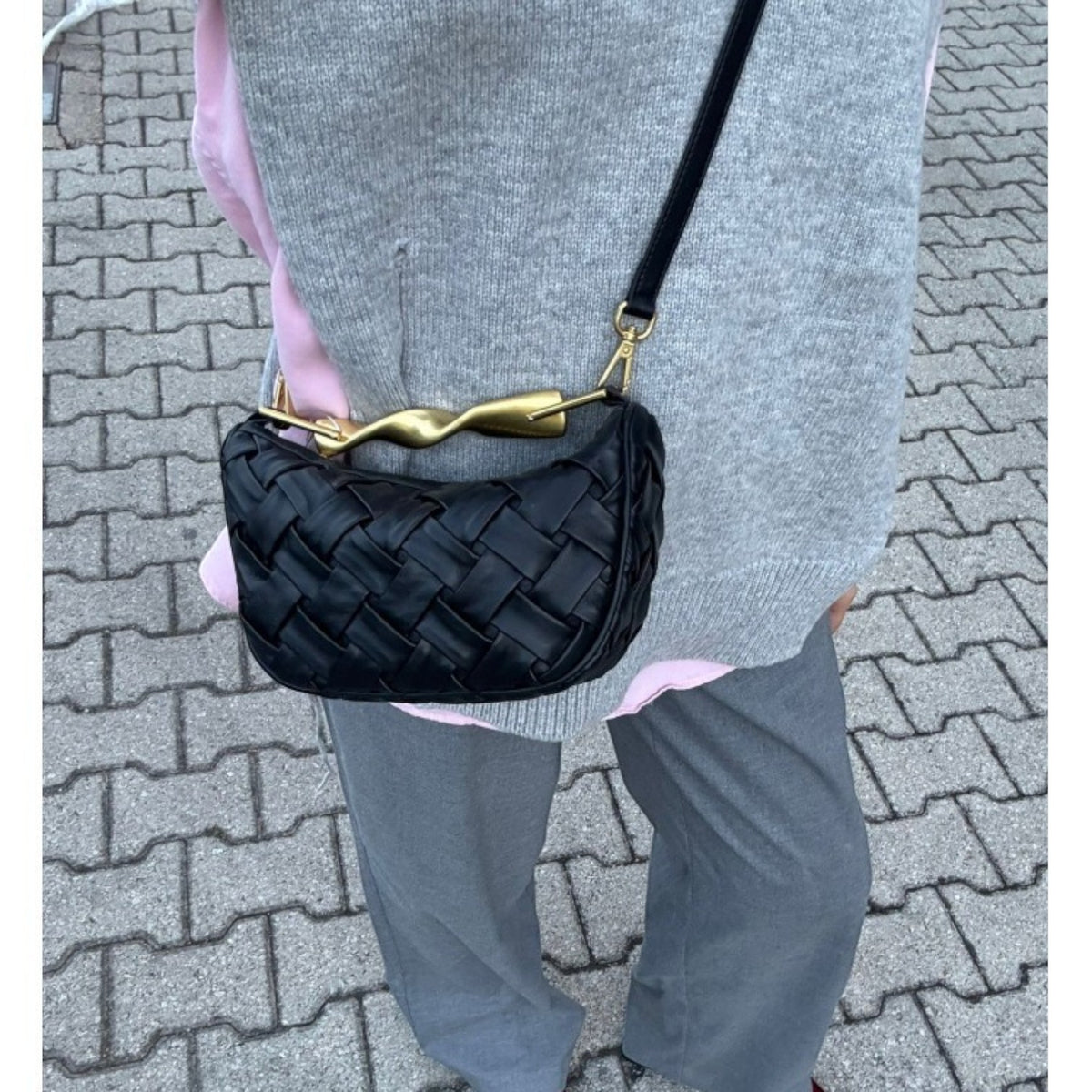 ShoeShop black woven leather shoulder bag with a unique gold metal handle detail worn over a grey sweater