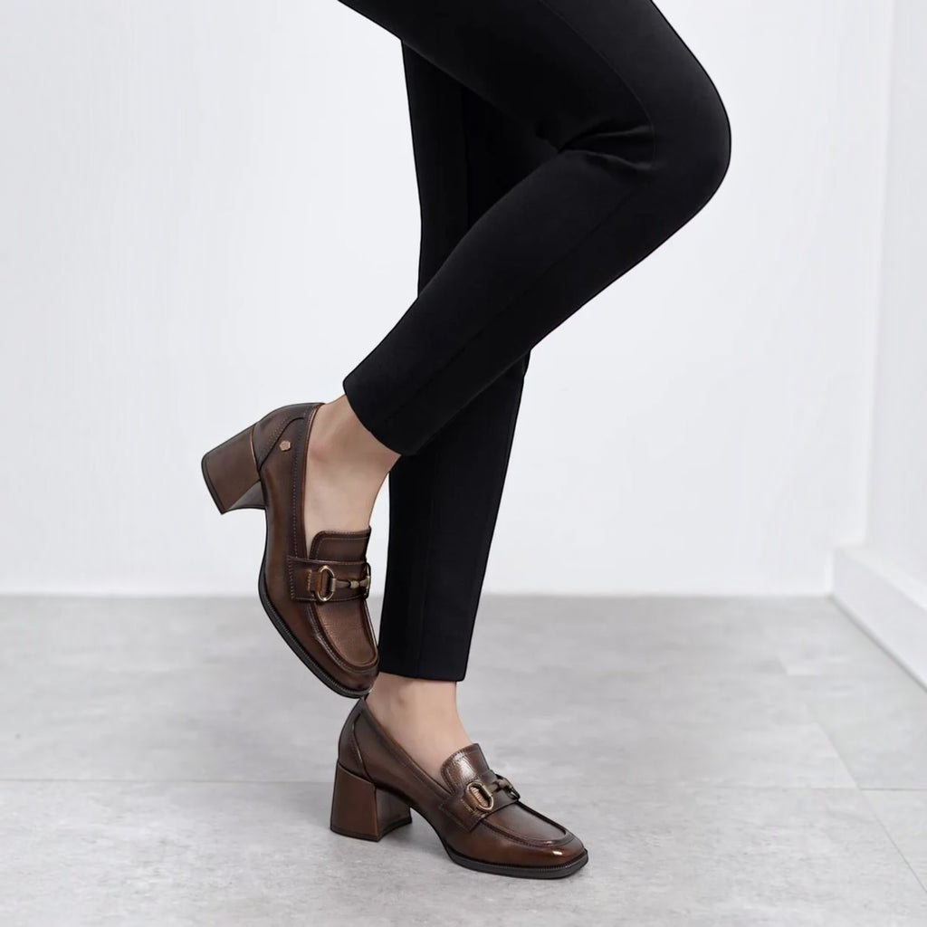 ShoeShop Carmela 162536 brown leather block-heel loafers with gold-tone horsebit detail worn with black trousers.
