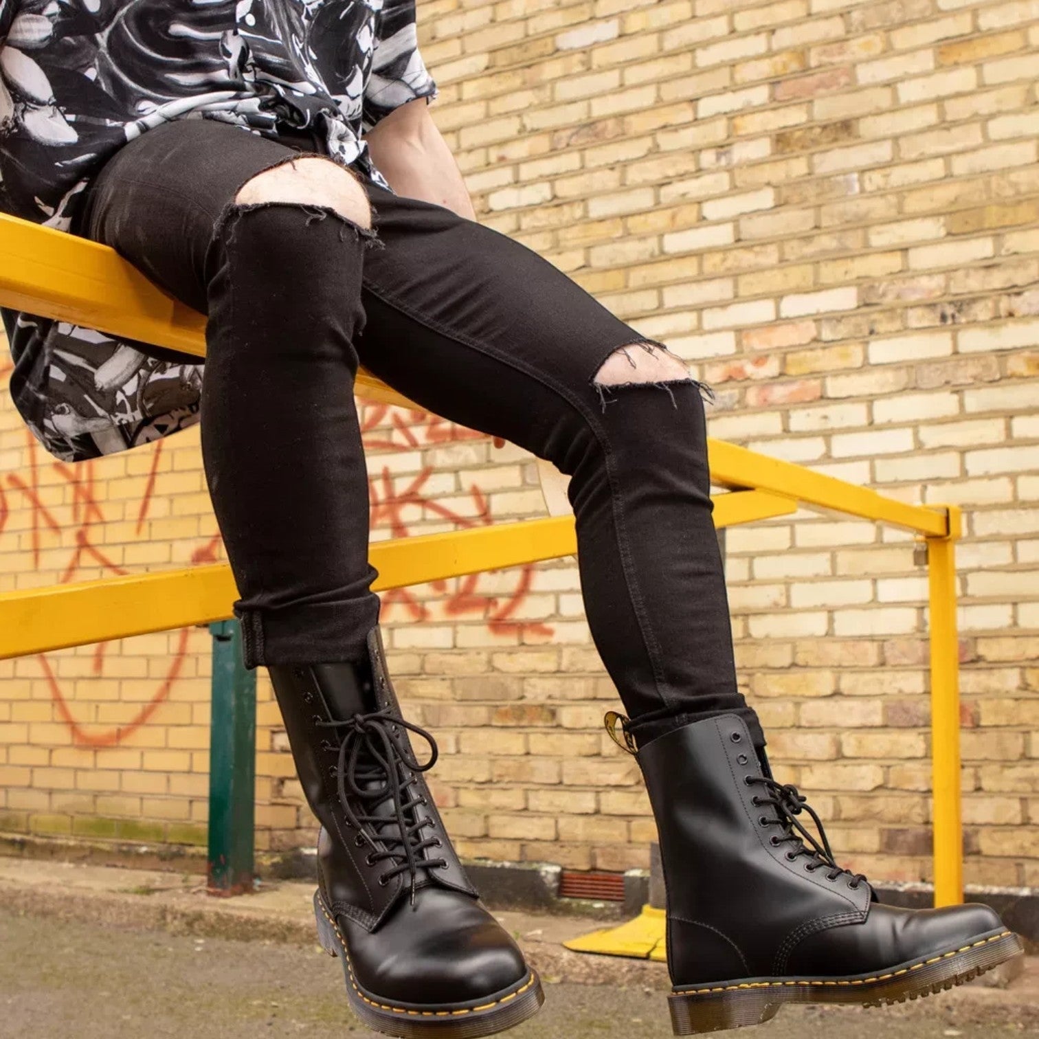 ShoeShop Dr. Martens 11857001 black patent leather lace-up boots with yellow stitching worn by a man
