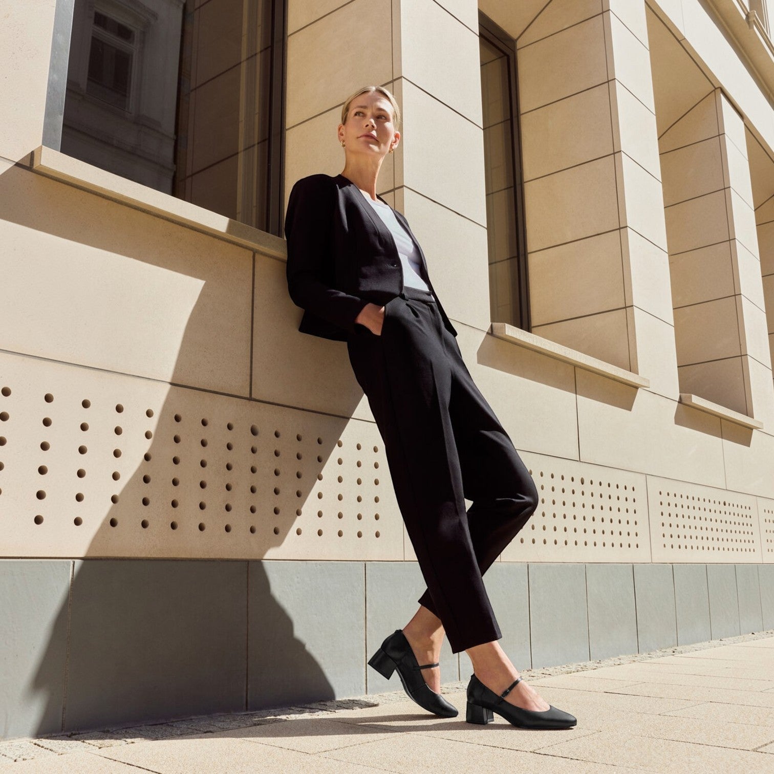 ShoeShop Tamaris black block heel mary jane shoes worn by a woman in a professional suit leaning against a building